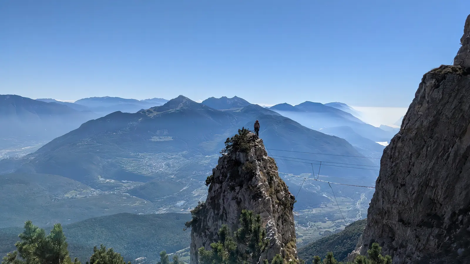 A climber moving across an exposed alpine via ferrata high above a green valley.